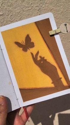 a person holding up a piece of paper with a shadow of a cat and butterfly on it