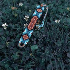 a blue and orange beaded bracelet laying on top of some green grass next to white flowers