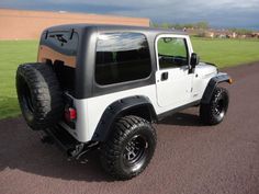 a white jeep parked on the side of a road next to a grass covered field