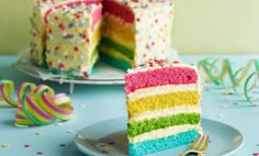 a slice of rainbow cake on a plate with the rest of the cake behind it