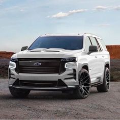 the front end of a white suv parked on top of a dirt field