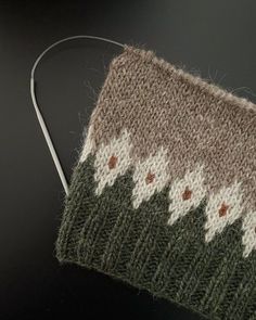 a close up of a knitted object on a black surface with white and brown designs