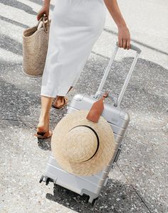 a woman walking down the street with her suitcase and hat on it's wheels