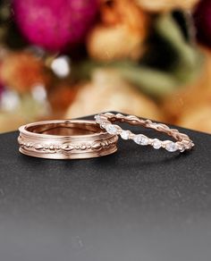 two wedding rings sitting on top of a black table next to some pink and white flowers