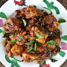 a white plate topped with meat covered in sauce and greens on top of a wooden table