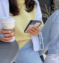 a woman sitting on a bench holding a cup of coffee and cell phone in her hand