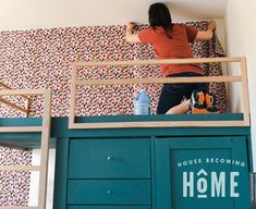 a woman standing on top of a bunk bed next to a blue dresser and ladder