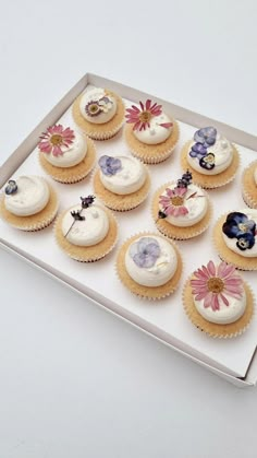 twelve cupcakes with white frosting and colorful flowers on them in a box