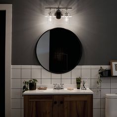 a bathroom with a round mirror above the sink and wooden cabinet below it, along with potted plants