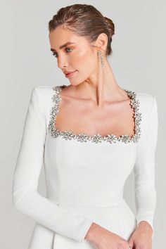 a woman wearing a white dress with long sleeves and beading on the neckline