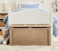 a teddy bear sitting on the floor next to a bed with white headboard and foot board