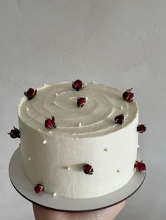 a hand holding a cake with white frosting and red roses on it's side