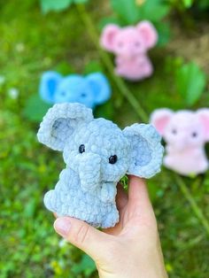 a hand holding a small stuffed elephant in front of several smaller ones on the grass