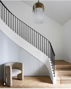 a white staircase with a chandelier hanging from the ceiling next to a wooden floor