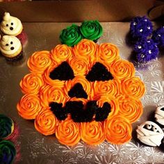 cupcakes with icing and decorations are arranged in the shape of a pumpkin