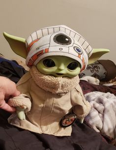 the baby yoda doll is wearing a star wars hat and holding something in its hand