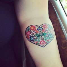 a heart shaped tattoo with colorful flowers on the arm