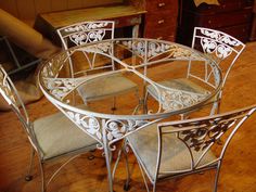 a glass table with four chairs around it on a wooden floor next to a dresser