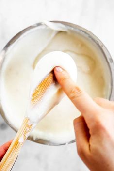 a person holding a wooden spoon with some liquid in it and another hand reaching for something