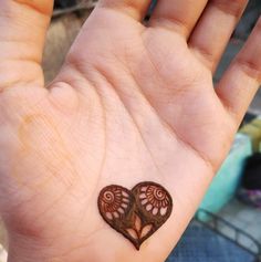 a small heart tattoo on the palm of someone's left hand, which is decorated with intricate designs