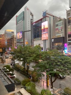 a city street filled with lots of tall buildings next to trees and people walking on the sidewalk