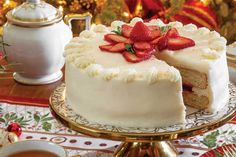 a white cake with strawberries on top is sitting on a table next to a cup of coffee