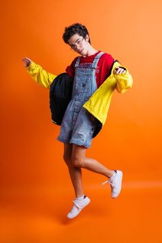 a boy in overalls and a yellow jacket is posing for the camera with an orange background