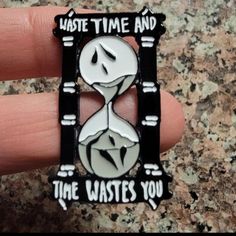 a hand holding a black and white lapel with an hourglass on it that says, waste time and the wastes you