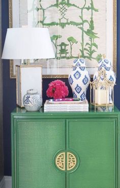 a green cabinet with blue and white vases on top of it next to a lamp