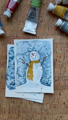 some watercolors are sitting on a table next to paint tubes, and a snowman