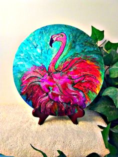 a pink flamingo sitting on top of a blue plate next to some green leaves