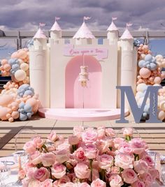 a table topped with lots of pink flowers next to a white castle and letter m