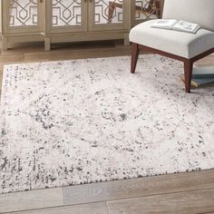 a white chair sitting on top of a wooden floor next to a large rug in front of a window