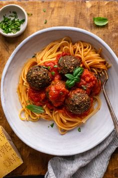 a white bowl filled with spaghetti and meatballs on top of a wooden cutting board