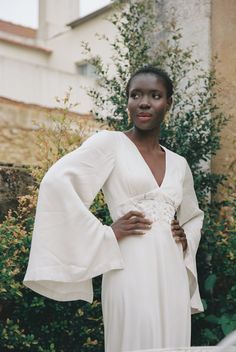 a woman in a white dress standing next to bushes