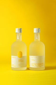 two bottles of liquid sitting next to each other on a yellow background with no one around them