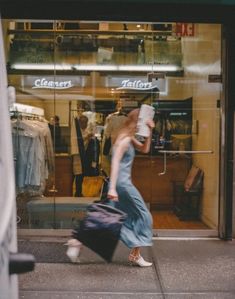 a woman walking past a clothing store holding a suitcase and carrying a cup in her hand