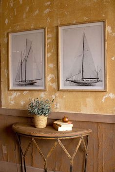 two framed pictures hang on the wall next to a table with a potted plant