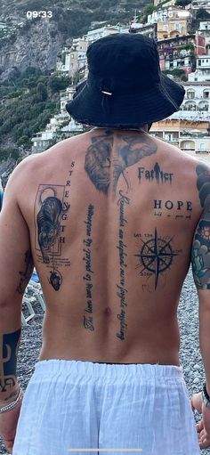 the back of a man with tattoos on his upper and lower half, standing in front of a beach