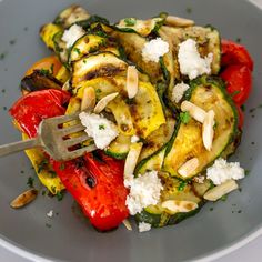 a plate with zucchini, tomatoes and feta cheese topped with a fork