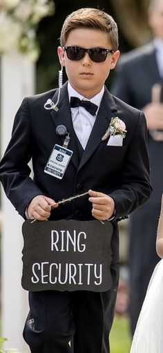 a young boy in a tuxedo holding a ring security sign