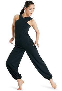 a woman in black jumpsuits is posing with her hands behind her back and one foot on the ground