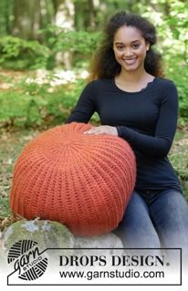 a woman sitting on top of a rock with an orange knitted ball in front of her