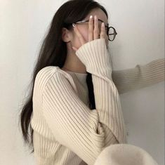 a woman with glasses covering her face while leaning against a wall and looking at the camera