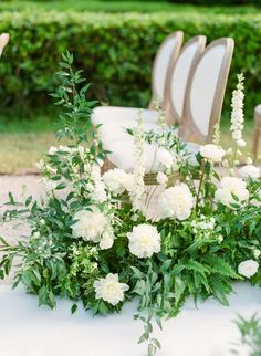 white flowers and greenery sit on an outdoor table set up for a wedding ceremony