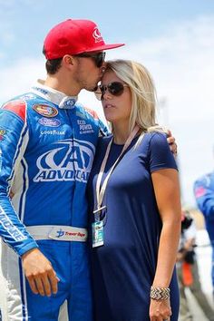 a man and woman standing next to each other in front of a race car on the track