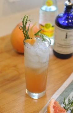 grapefruit and rosemary garnish in a glass next to an orange slice on a cutting board