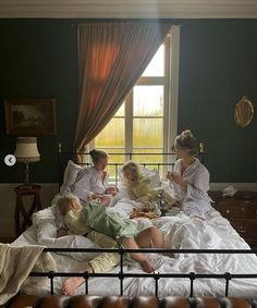 three women and two children sitting on a bed in front of a window with curtains