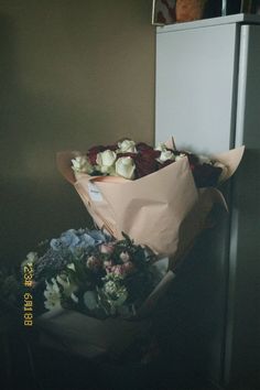 two bouquets of flowers sitting on top of a table in front of a refrigerator