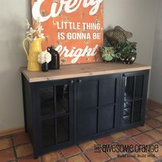 an orange sign sitting on top of a wooden cabinet next to a vase and potted plant